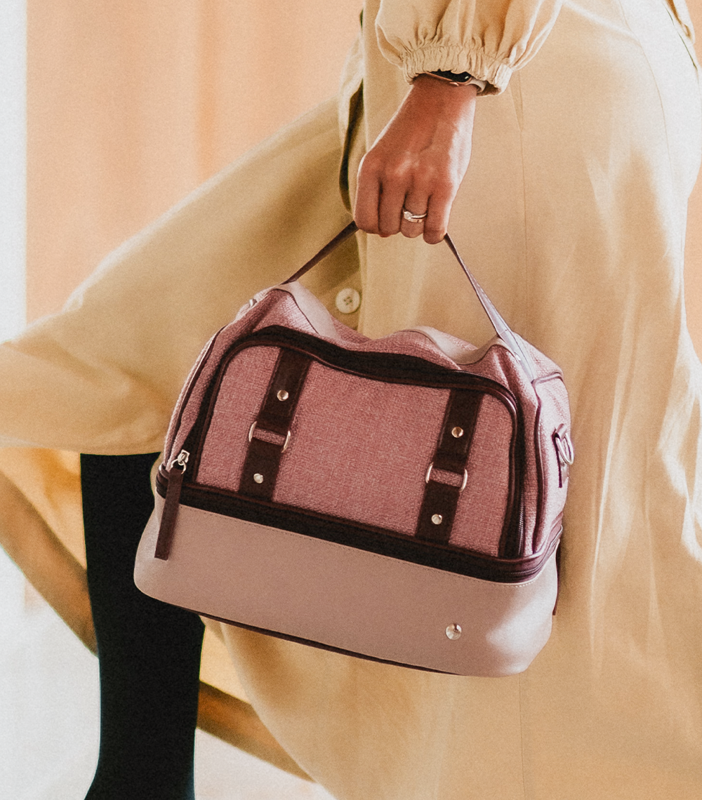 Mulher caminhando e segurando uma bolsa térmica vermont da PACCO de duas cores nos tons de rosa e vinho.