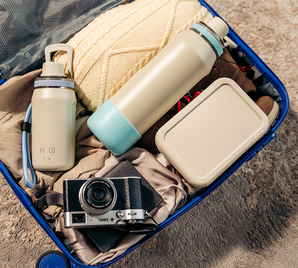 Produtos PACCO ideais para viagem: garrafas térmicas, pote de silicone e acessórios sustentáveis organizados em uma mala pronta para a aventura.