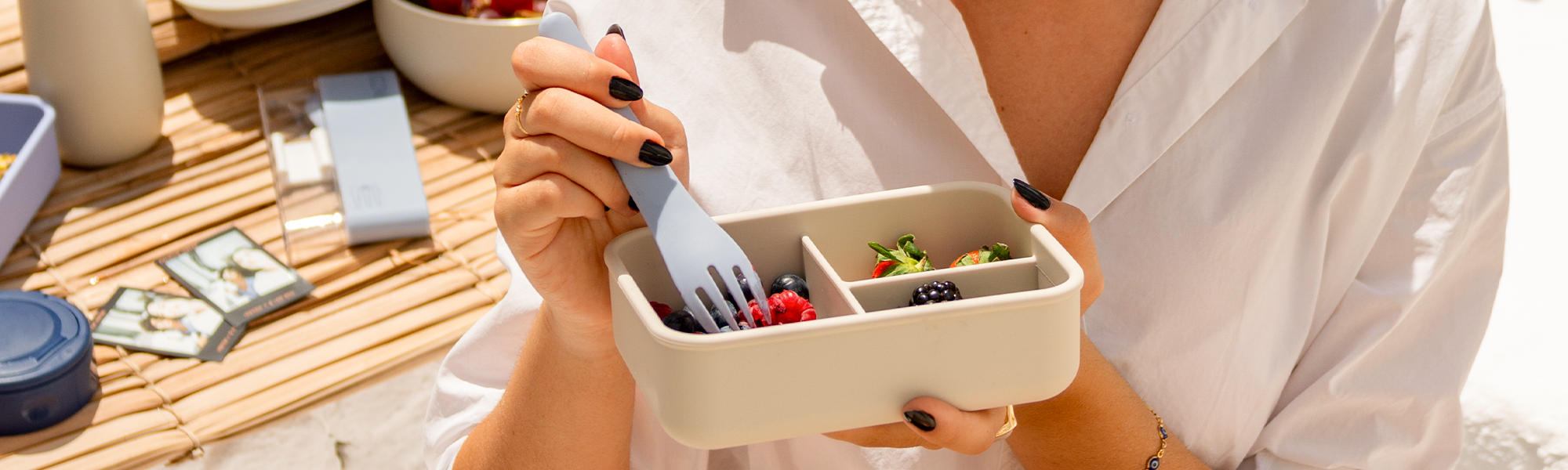 Mulher usando talher da PACCO para comer frutas em um pote de silicone com divisórias.