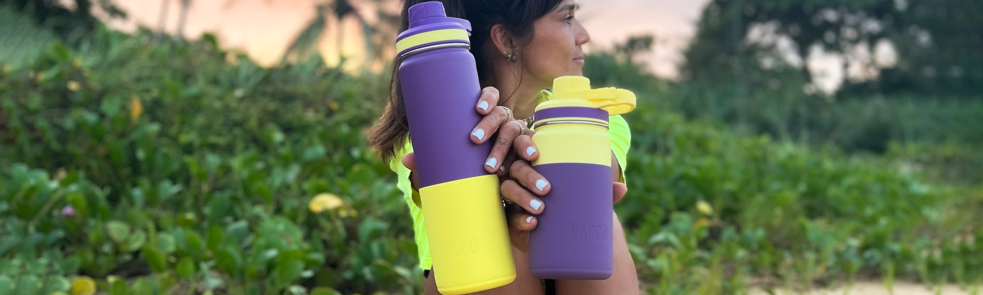 Mulher na praia exibindo a personalização das suas garrafas térmicas PACCO, combinando capas de silicone e tampas de cores diferentes.