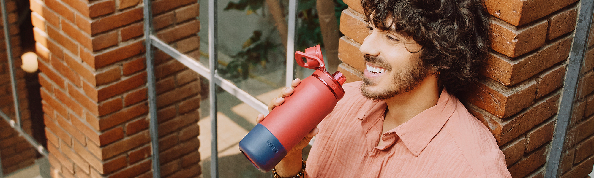 Homem sorrindo segurando uma garrafa térmica PACCO pitanga, personalizada com a Capa de Silicone Vyta na cor açaí.