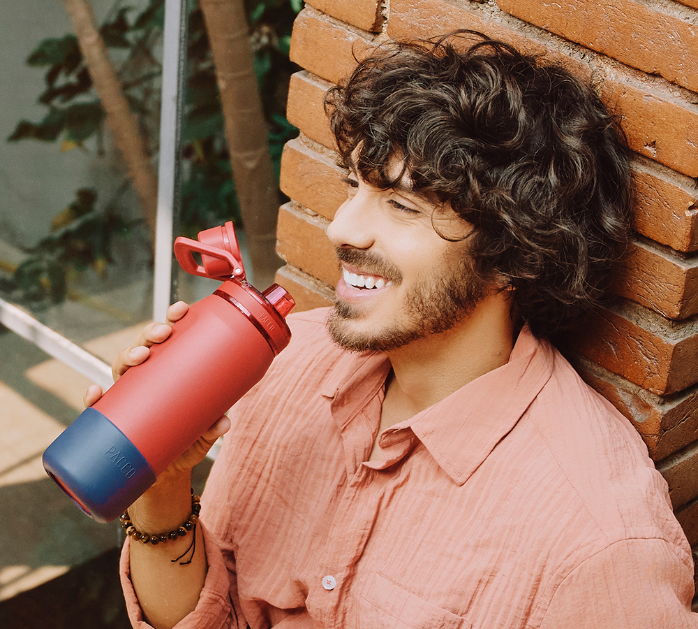Homem sorrindo segurando uma garrafa térmica PACCO pitanga, personalizada com a Capa de Silicone Vyta na cor açaí.