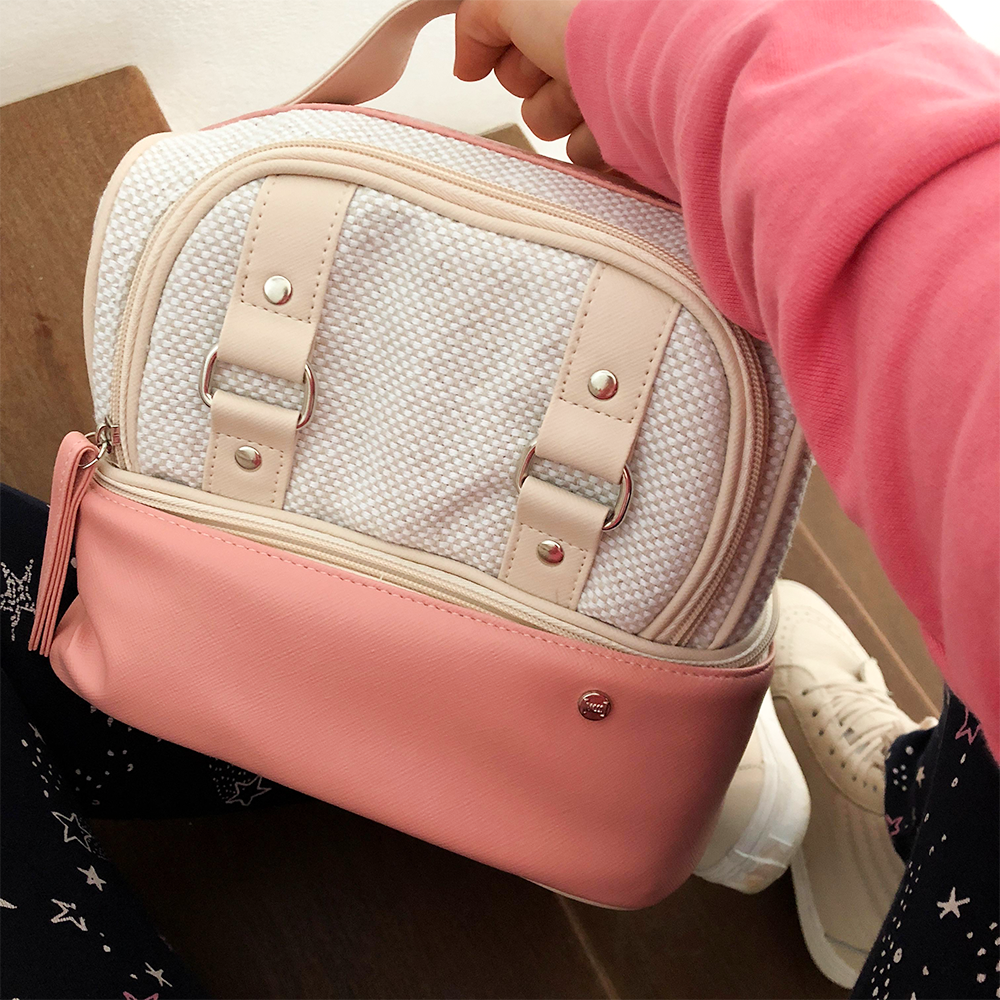 Pessoa sentada em uma escada de madeira, segurando a bolsa térmica Vermont Mini com base rosa e parte superior em tecido texturizado.