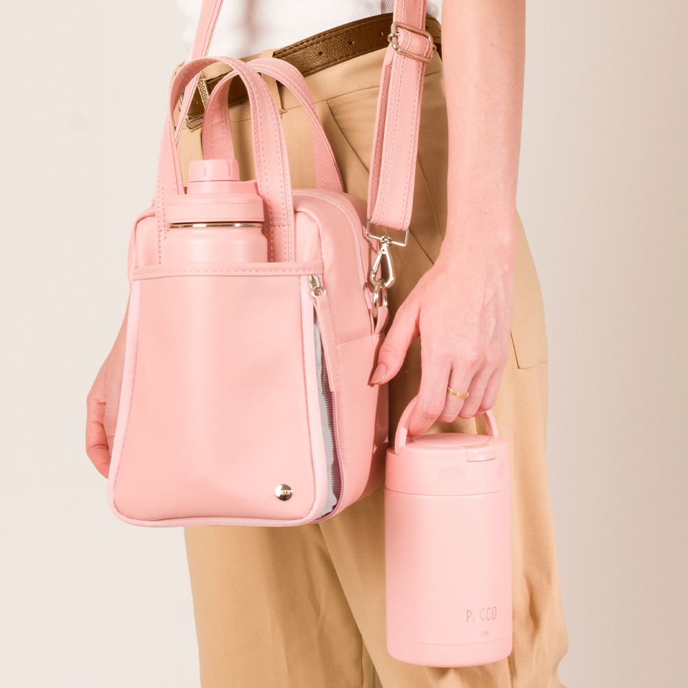 Mulher carregando um conjunto de produtos na cor rose: uma bolsa térmica com garrafa e um pote térmico da PACCO na mão.